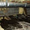 Fiberglass insulation dripping off a floor joist in a soaked crawl space with a think black liner in Milwaukee.